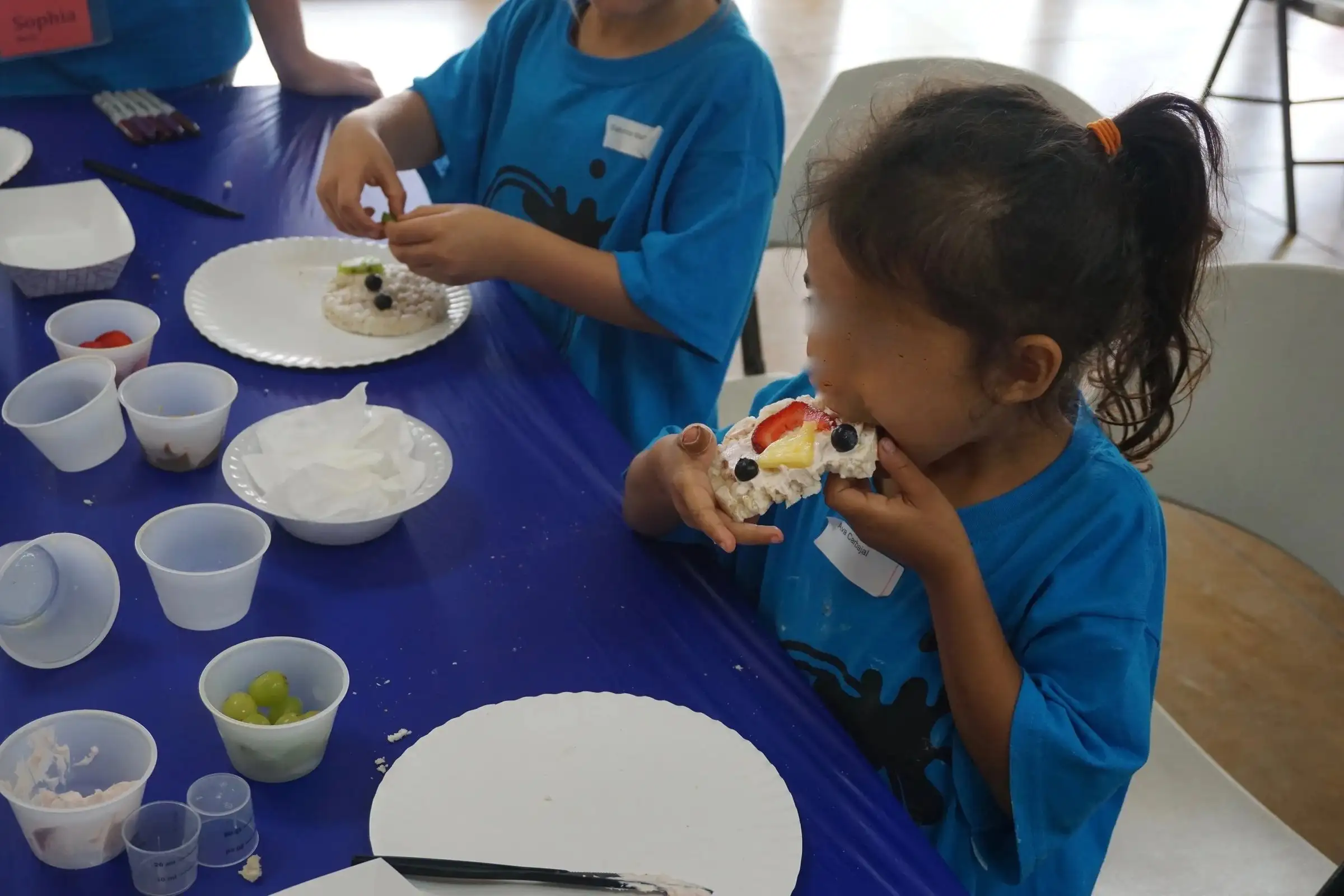Children in matching blue shirts working on crafts with volunteers at summer camp