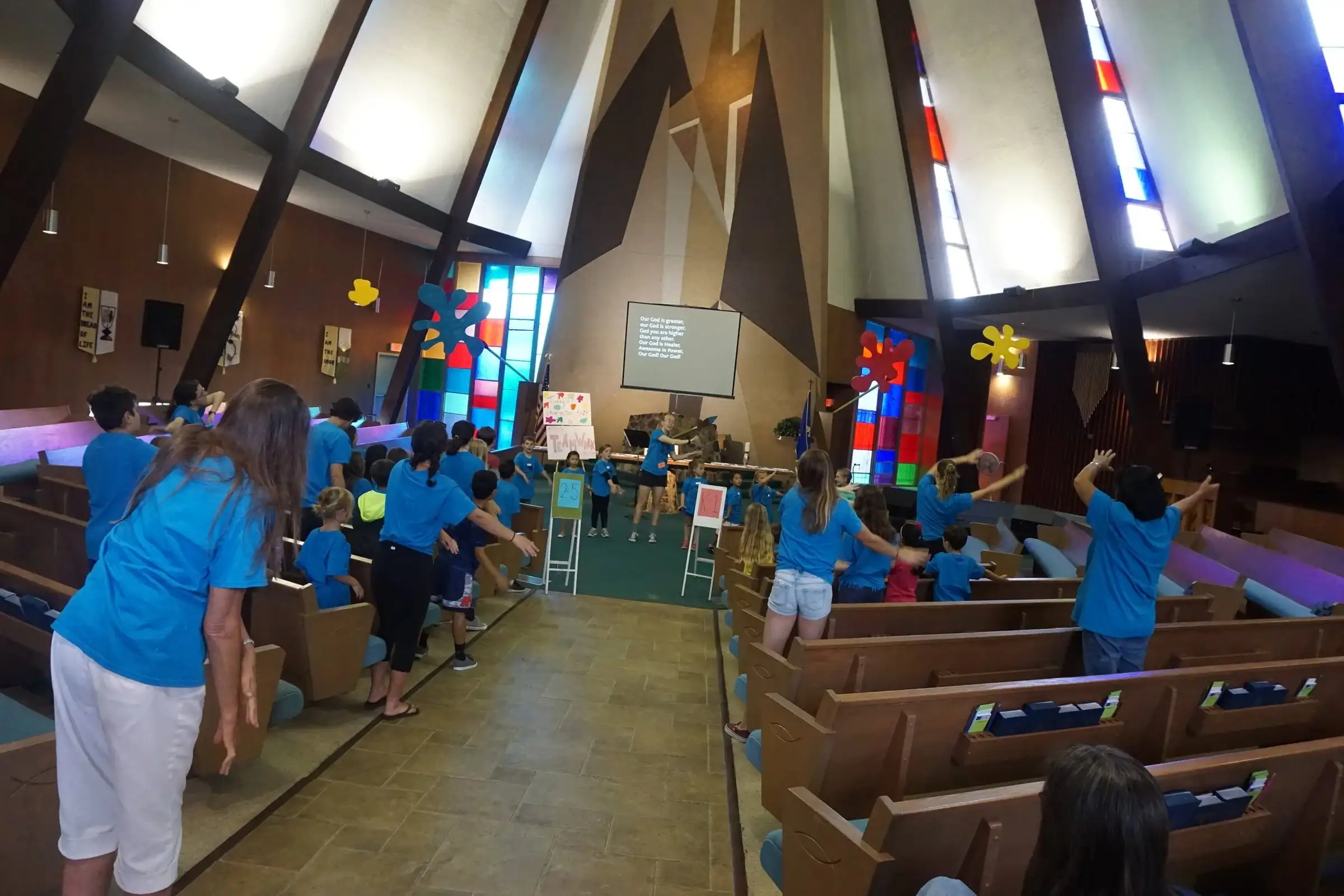 Kids in blue camp shirts dancing in the aisle of the sanctuary during summer camp