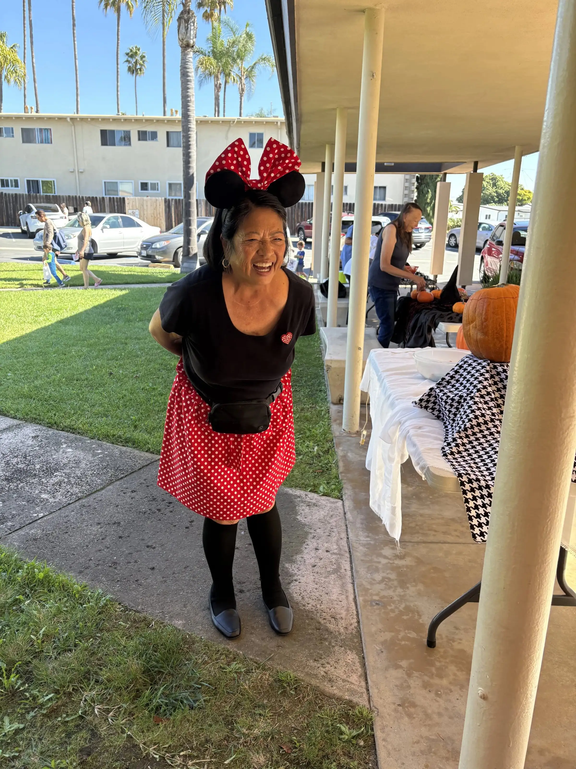 A smiling volunteer in Minnie Mouse ears and a polka-dot skirt on the church lawn