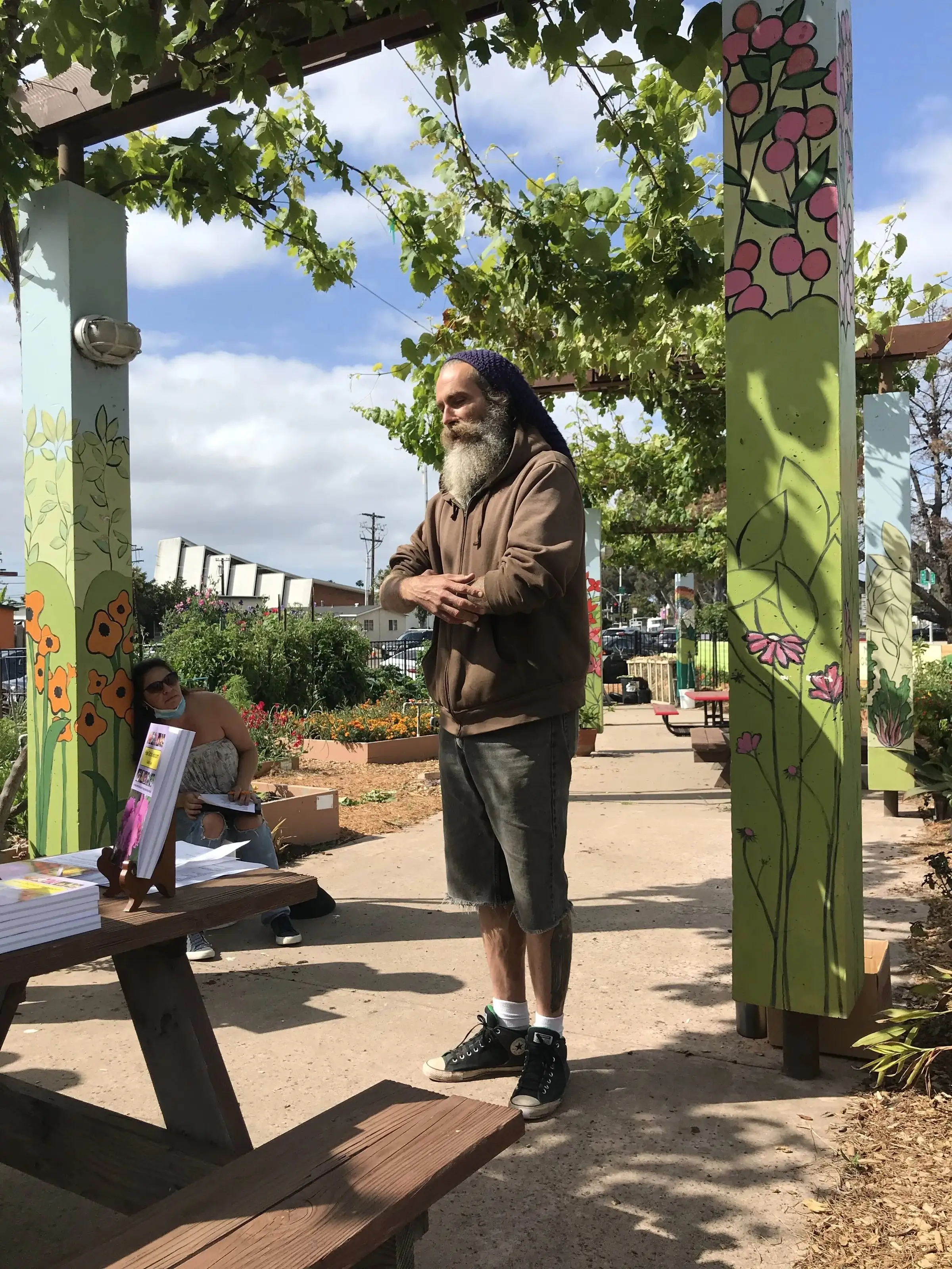 A guest speaker addresses gardeners beneath the vine-covered arbor