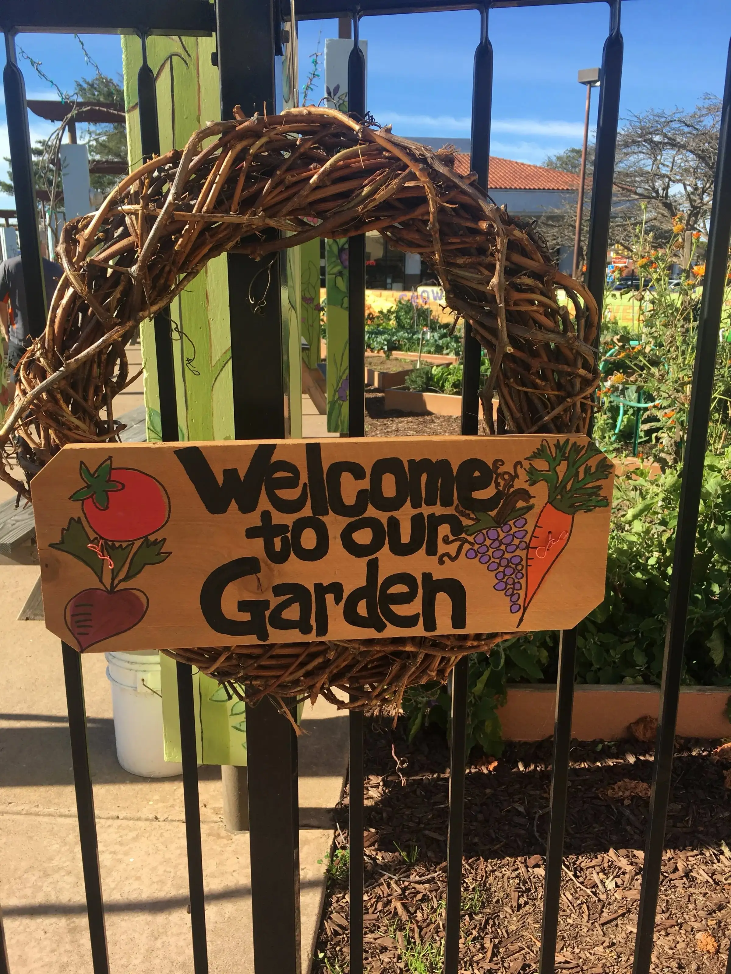 A “Welcome to our Garden” sign hanging in a grapevine wreath on the gate