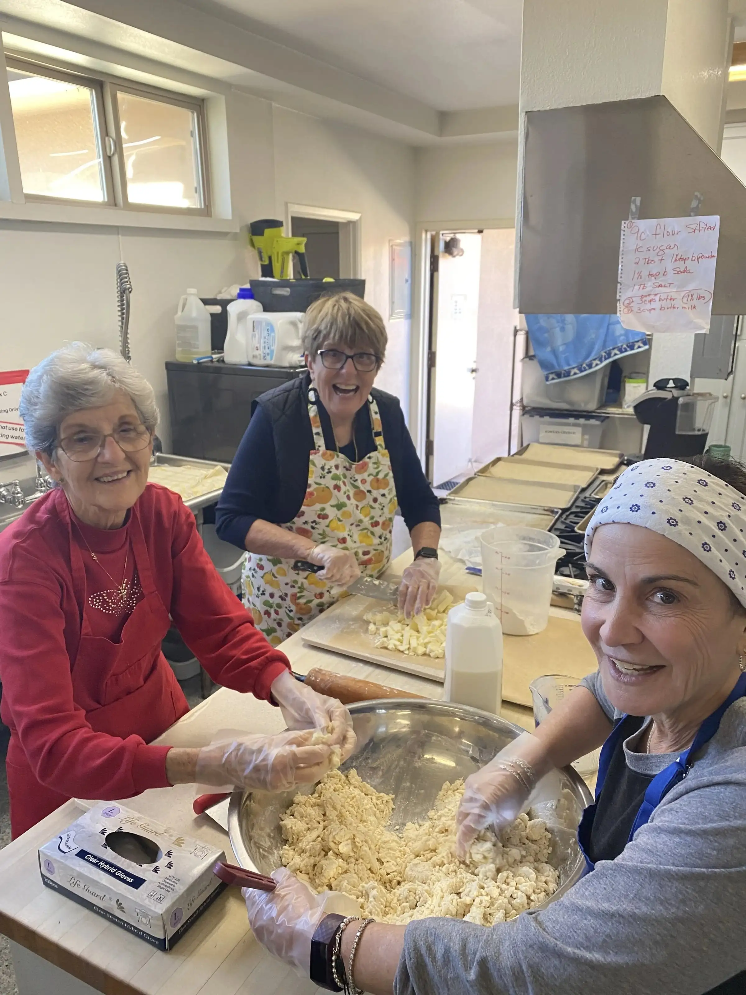 Three women laughing together while preparing food in the church kitchen