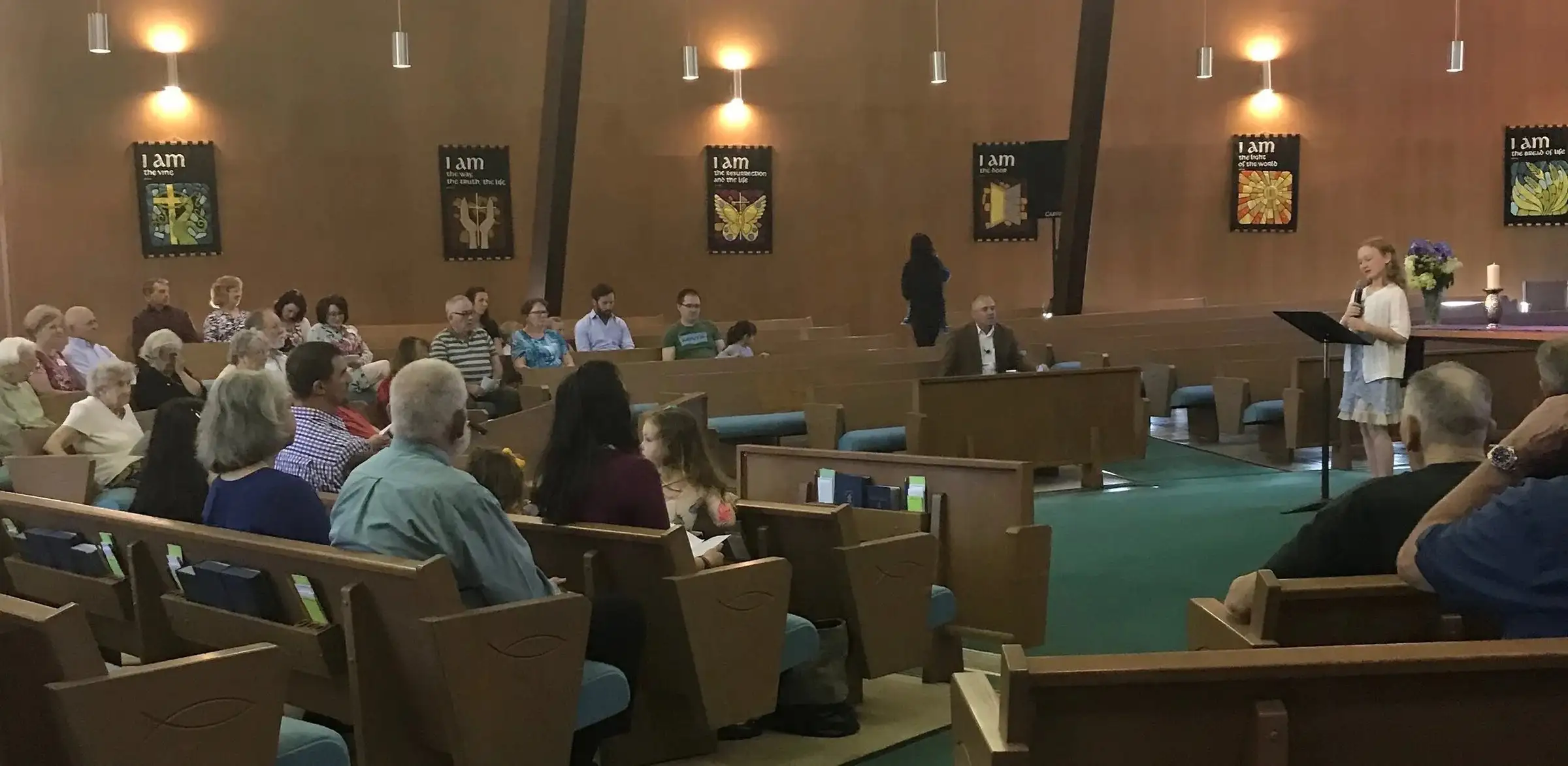 A young girl reads scripture at the lectern while the congregation listens