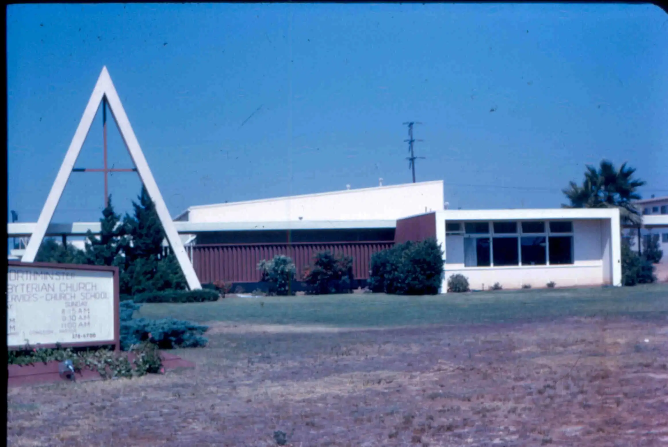 The first church building with its tall A-frame marker against a blue sky