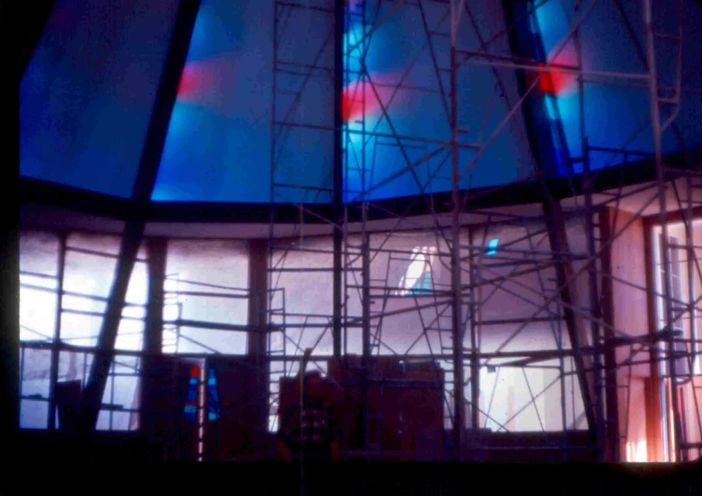 Scaffolding inside the sanctuary with blue and red stained glass glowing above